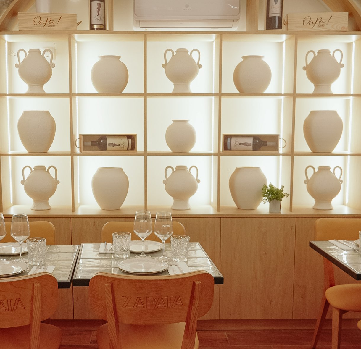Salle avec étagère éclairée de cruches en terre cuite et tables dressées